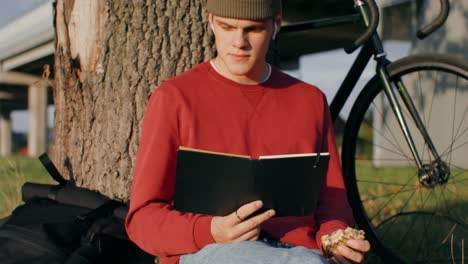 Young man reading and eating a sandwich in a park