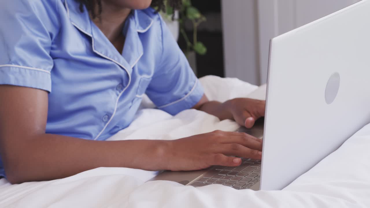 Hands are typing on white laptop on bed, reading screen content and smiling while replying