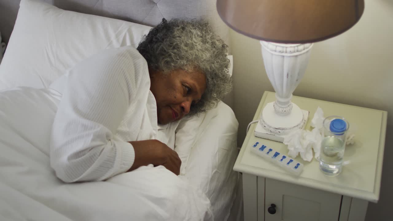 Sick senior african american woman reaching out for tissues while lying on the bed at home