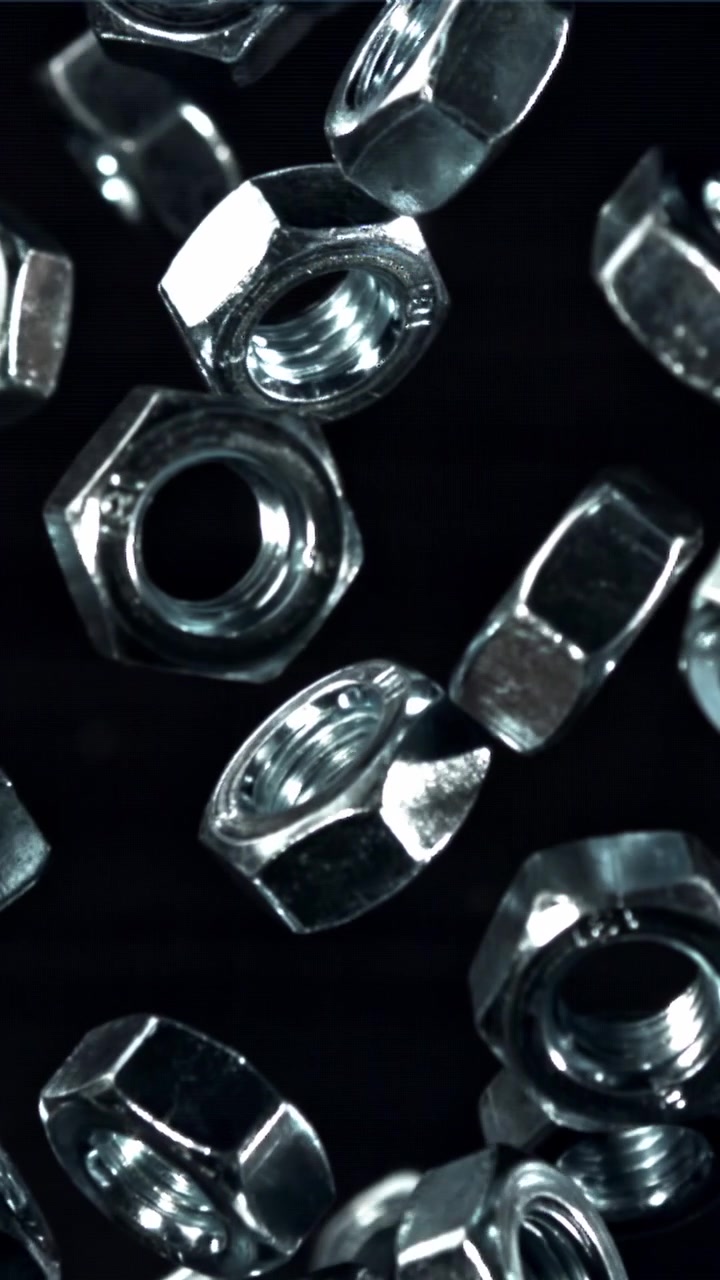 Glänsande metallmuttrar faller i slow motion på svart bakgrund