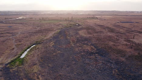 a completely barren landscape shows only some vegetation around a waterhole