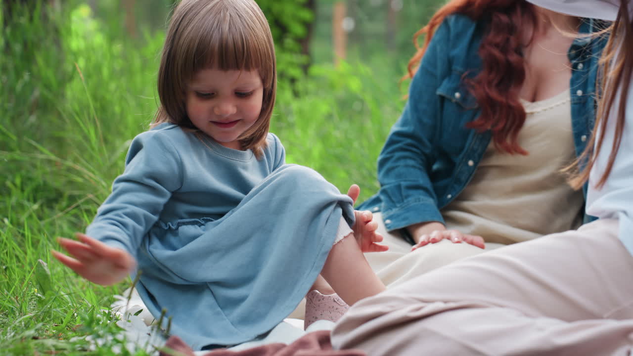 푸르른 녹색 숲으로 둘러싸인 야외에서 형제자매, 장난기 넘치는 엄마와 함께 돗자리에 앉아 웃음, 미소, 사랑을 나누며 따뜻한 가족 간의 유대감을 즐기는 행복한 아이