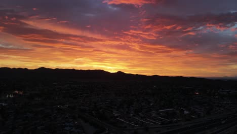 aerial view of fiery sunset behind mountains, orange yellow and pink clouds