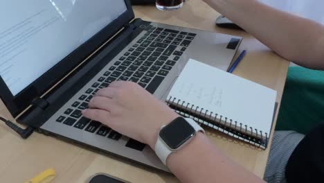 hands organizing thoughts, writing in a notebook alongside a laptop showing text