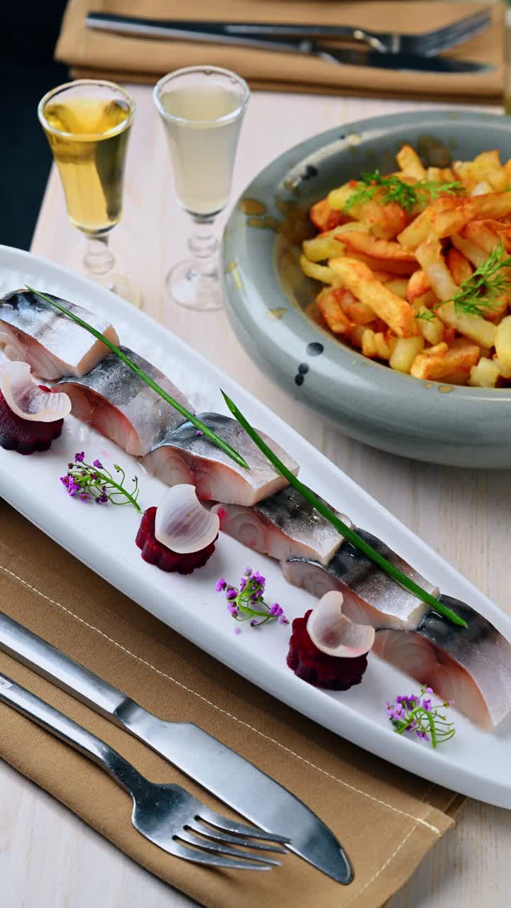 Bevægelsessløring af et sildefad, der serveres på bordet. Dynamisk billede af en hvid, rektangulær tallerken med fiskeanretning, der bevæger sig hen over et dækket bord med kartofler.