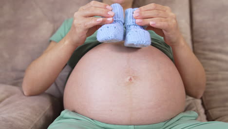 Bare stomach of a future mother. Pregnant woman playing with little knitted socks on her belly lovingly. Close-up.