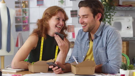 Männliche-Und-Weibliche-Modedesigner-Beim-Arbeitsessen-Und-Blick-Auf-Mobiltelefone-Im-Studio