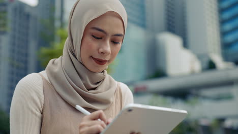 Woman in hijab using tablet in urban setting