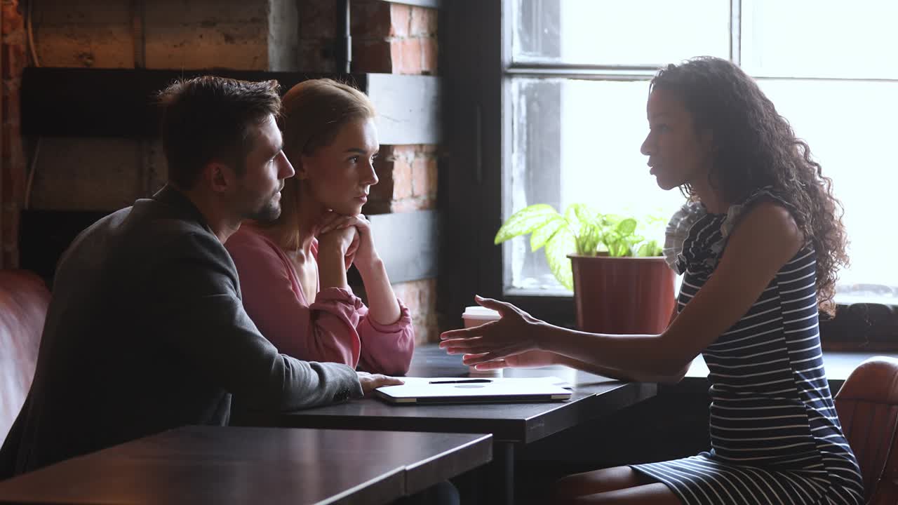 una vendedora africana consulta a una pareja de clientes sobre un acuerdo de seguro.