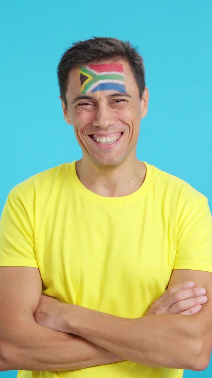 Homem de pé com a bandeira sul-africana pintada no rosto sorrindo