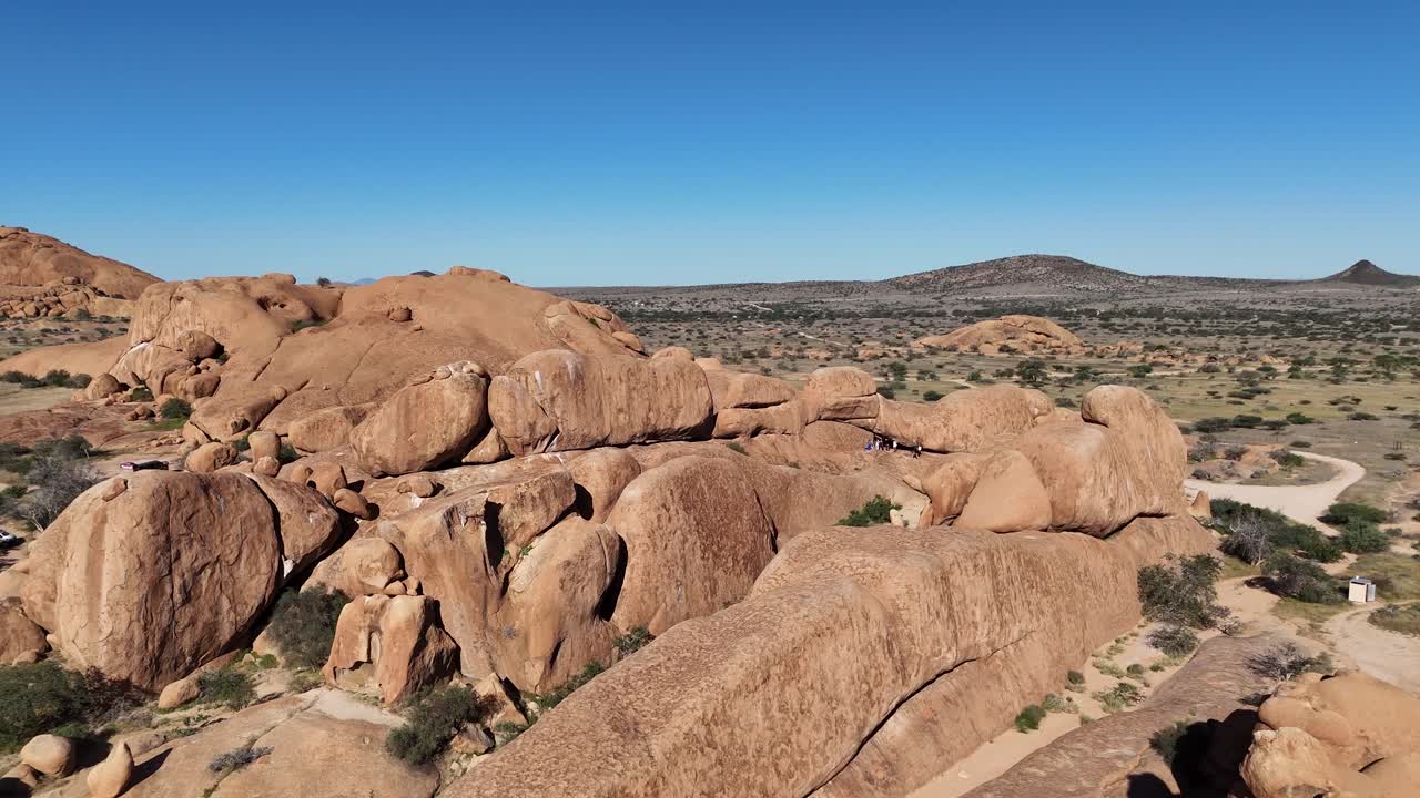 aerial view of Spitzkoppe mountain range in Namibia, surrounded by golden desert sands and expansive rock formations under a blue sky