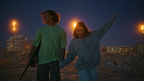 relaxed teen pair walking at evening sandy beach. musician man holding guitar