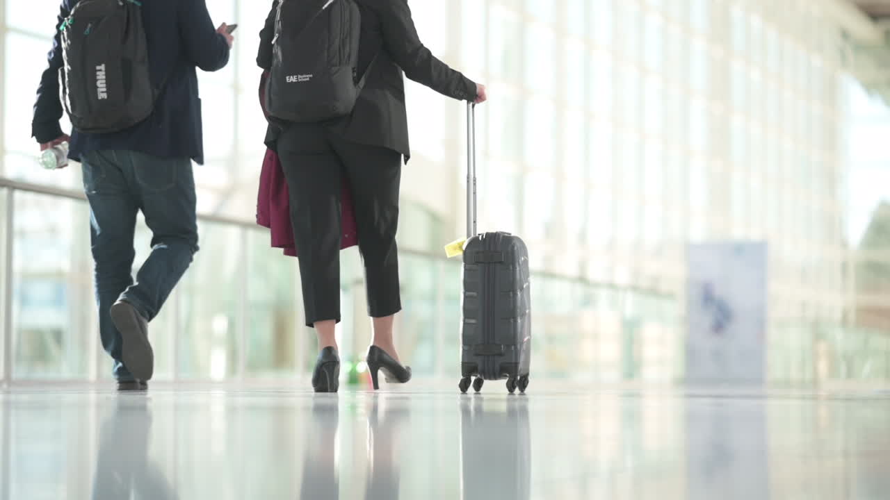 People in business outfits walking with luggage in a bright hall