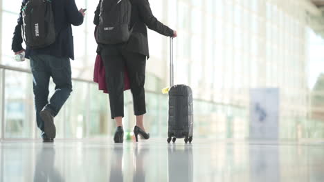 people in business outfits walking with luggage in a bright hall