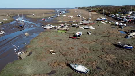 various stranded abandoned fishing boat wreck shipyard in marsh mud low tide coastline aerial view pull back