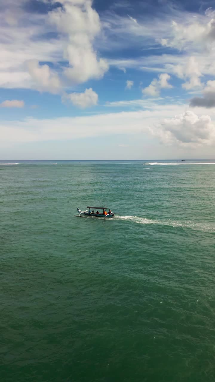 A vertical drone captures traditional Balinese boats smoothly moving across the calm sea in the early morning light creating a serene and peaceful coastal atmosphere.