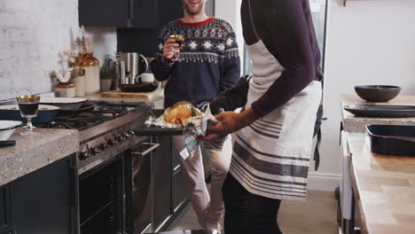 Homosexuelles-Männliches-Paar-Zu-Hause-In-Der-Küche,-Das-Am-Weihnachtstag-Das-Abendessen-Kocht-Und-Hühnchen-Aus-Dem-Ofen-Nimmt