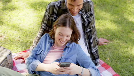 happy diverse couple having picnic and using smartphone in sunny garden, in slow motion