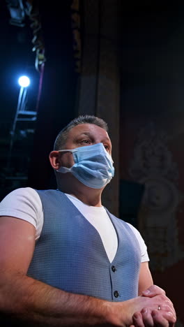 actor in medical mask talking. man is standing on stage in theater at spotlights and speaking during pandemic. view from below. vertical video