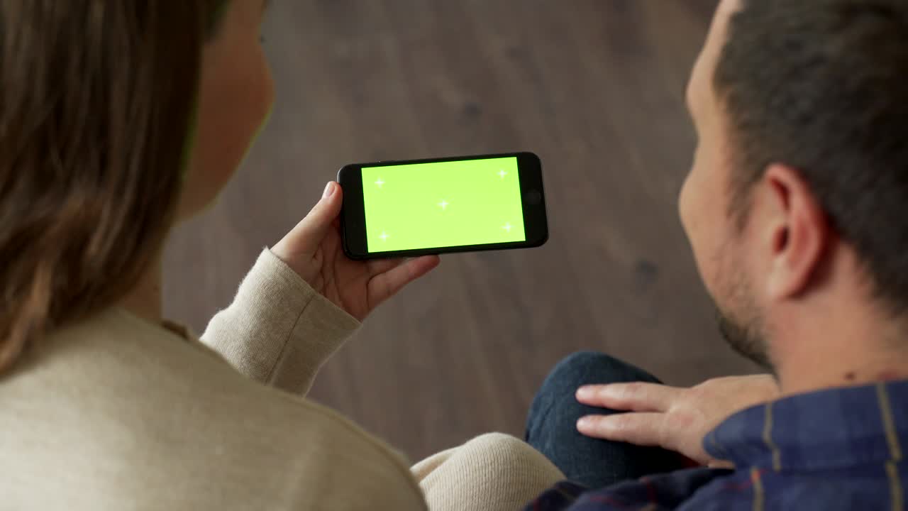 인터넷과 소셜 미디어를 위해 녹색 화면의 드폰을 사용하는 젊은 부부. 녹색 모니터의 스마트폰을 들고 있는 남자와 여자