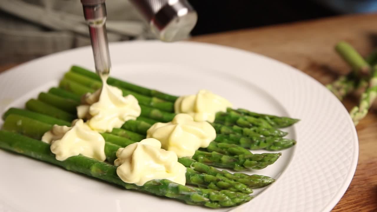 Chef che applica salsa cremosa sulle punte di asparagi verdi freschi