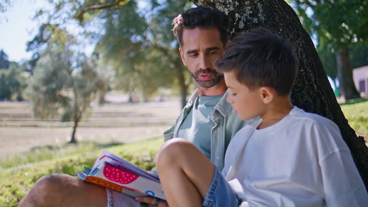 Man boy watching book gathering in cozy park nature closeup. Parent kid talking