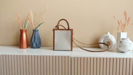bolsa de cuero tejida blanca en un estante blanco con jarrones y flores secas