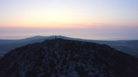 aerial - flying from front to behind the man standing on top of the mountain watching beautiful sunset-sunrise over the peaks