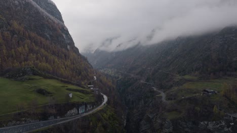 Calm-beautiful-backwards-flying-drone-video-in-Swiss-Alps-valley-on-moody-grey-winter-afternoon-with-lush-pine-forests-and-clouds-in-mountains