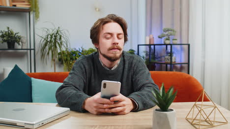 Caucasian bearded man sitting at table use smartphone share messages on social media application