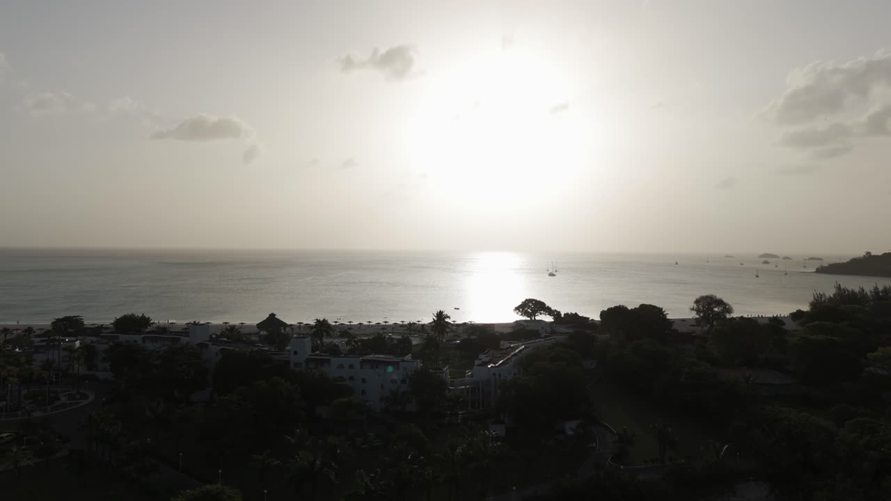 Sunset view over Jolly Harbor Antigua with silhouetted trees and calm water under a hazy sky