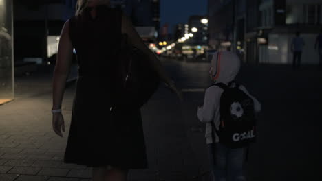 Vista-En-Cámara-Lenta-De-Una-Mujer-Con-Su-Hijo-Yendo-A-La-Calle-Peatonal-Vacía-De-Noche-Rotterdam-Países-Bajos