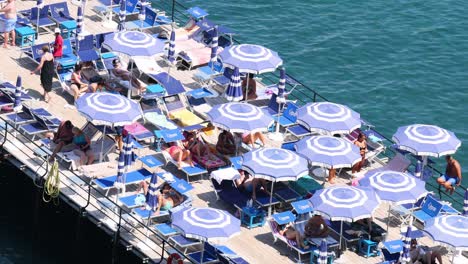 people sunbathing under umbrellas on a pier