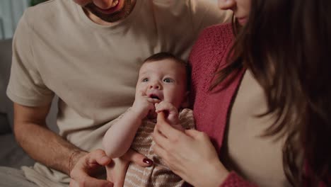 Nahaufnahme-Eines-Kleinen-Mädchens-In-Einem-Braunen-T-Shirt,-Das-In-Den-Armen-Ihrer-Jungen-Mutter-Liegt-Und-Sich-Umschaut,-Während-Eine-Junge-Familie-Zeit-Miteinander-In-Einem-Modernen-Apartment-Verbringt