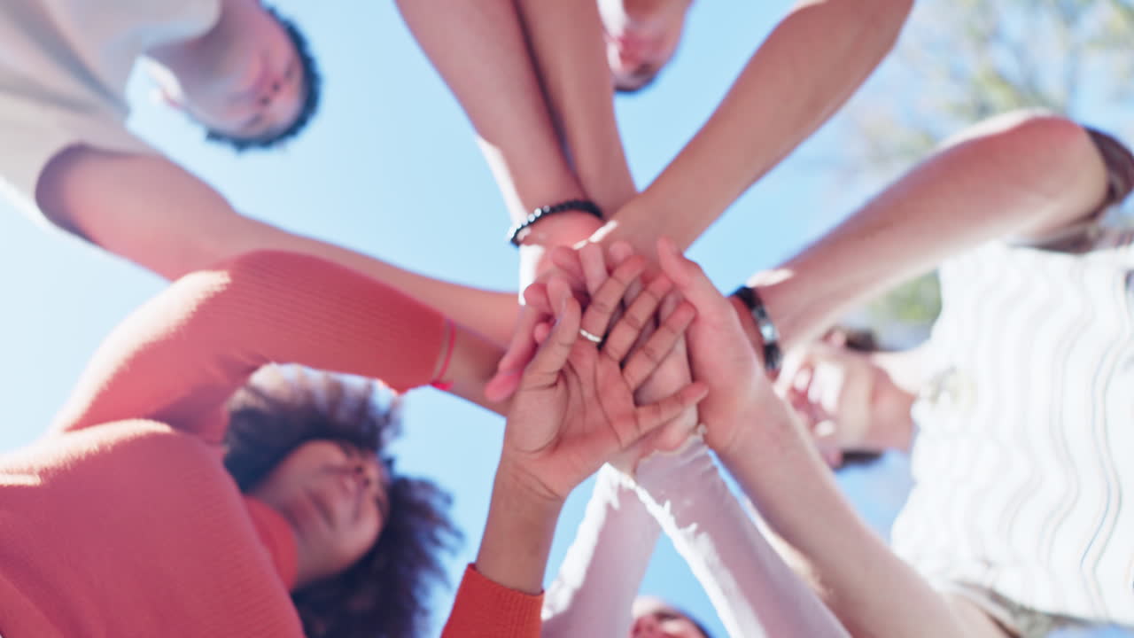 Group of people stacking hands together to symbolize teamwork and collaboration