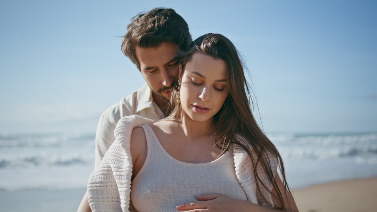 휴가 중 휴식을 취하는 해변에 서 있는 임신 중인 배우자의 초상화. 이 포옹하고 있다.