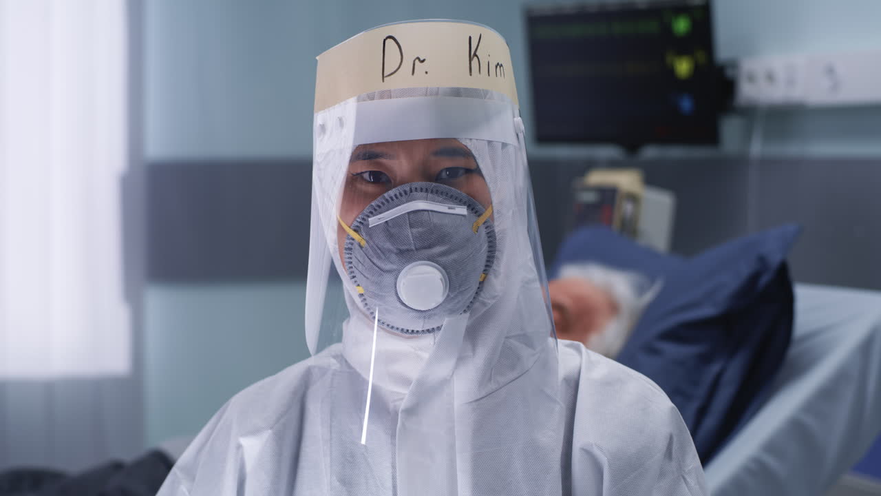 Doctor Kim in full PPE and face shield in a hospital setting with a patient in the background