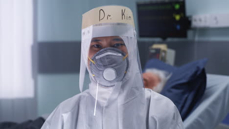 doctor kim in full ppe and face shield in a hospital setting with a patient in the background