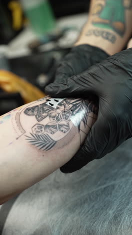 Vertical close up shot of tattoo artist applying adhesive protection to a new tattoo, interior