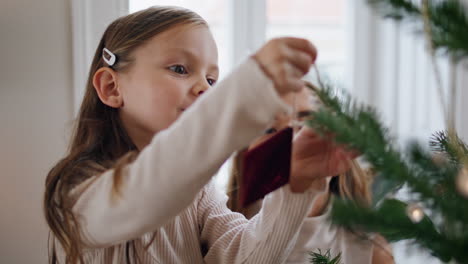 affectionate kid putting xmas toys on branches portrait. woman helping child