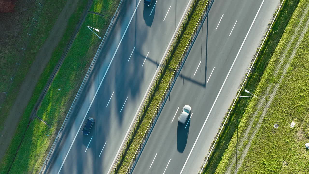 Aerial view of highway with three moving cars casting long shadows across clean asphalt lanes in daylight