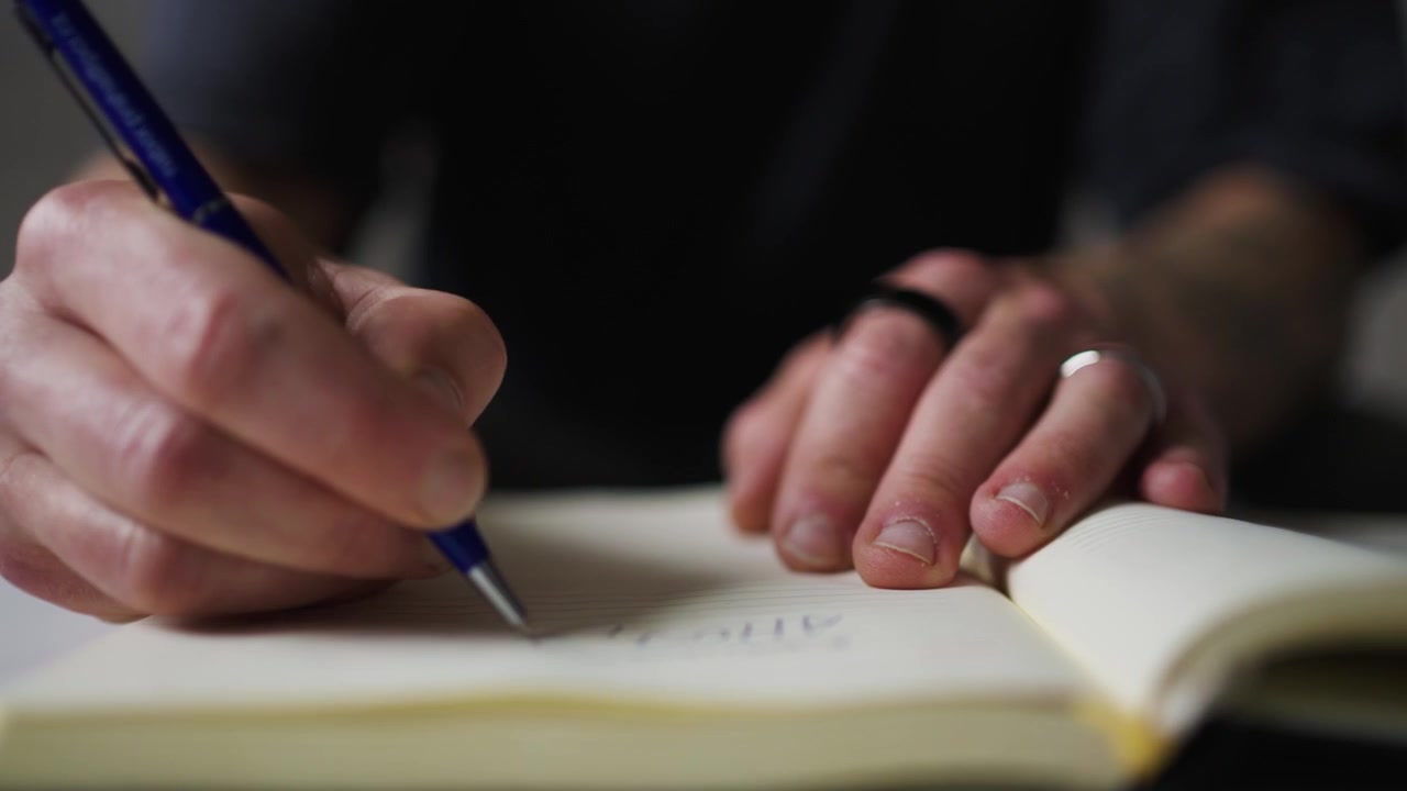 Close-up of man writing in a notebook with a pen.