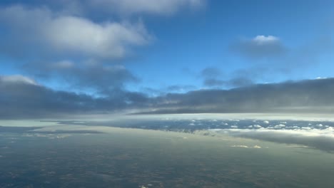 paisaje nublado pov disparado desde una cabina de un avión volando a través de un cielo azul con algunas nubes grises y amarillas en la hora dorada