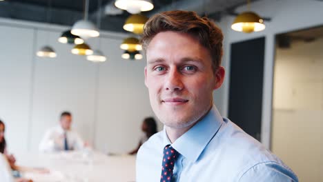 portrait of businessman in modern boardroom with colleagues meeting around table in background shot in slow motion