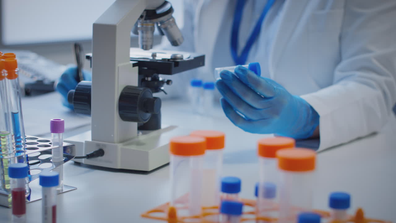 primer plano de un trabajador de laboratorio que realiza investigaciones utilizando un microscopio con un tubo de ensayo etiquetado sigma