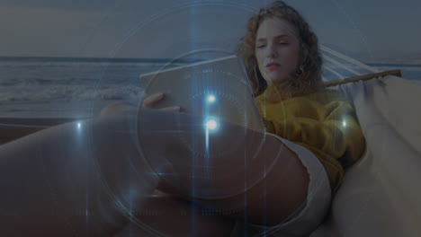animación de un haz de luz con un círculo sobre una mujer caucásica usando una tableta digital en una hamaca en la playa