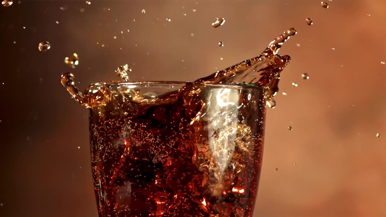 Cubitos de hielo salpicando en un vaso de cola refrescante en cámara lenta
