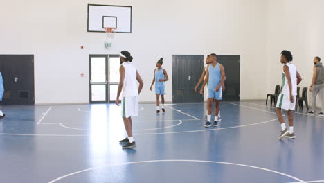 multiracial male basketball players playing basketball and passing basketball in gym