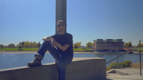 A-man-sits-on-a-ledge-overlooking-a-lake-and-takes-out-his-cellphone