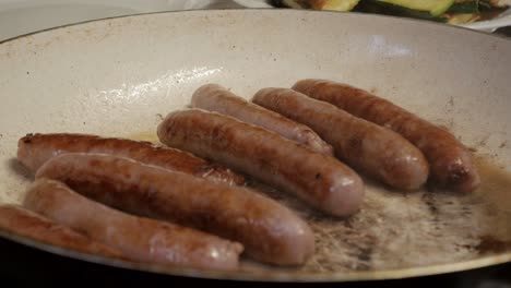 golden brown sausages sizzling in a frying pan with a hand turning them